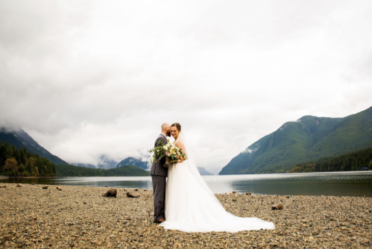 Bride and groom portrait by a lake with mountain backdrop