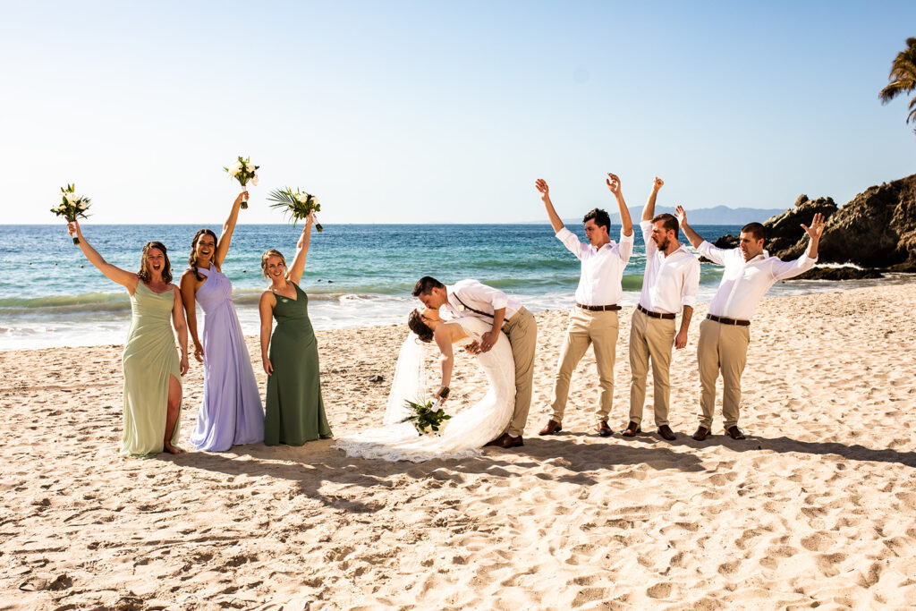 Group wedding photo on the beach in Cabo San Lucas with newlyweds kissing