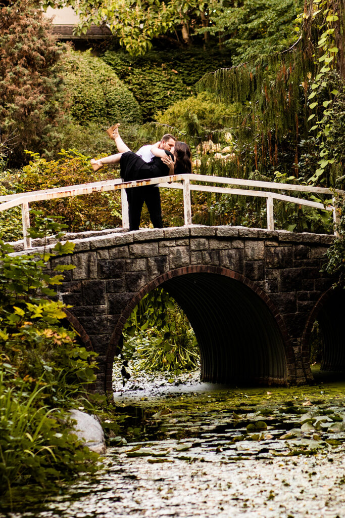 Couple kissing on a bridge surrounded by greenery during their engagement shoot in Vancouver