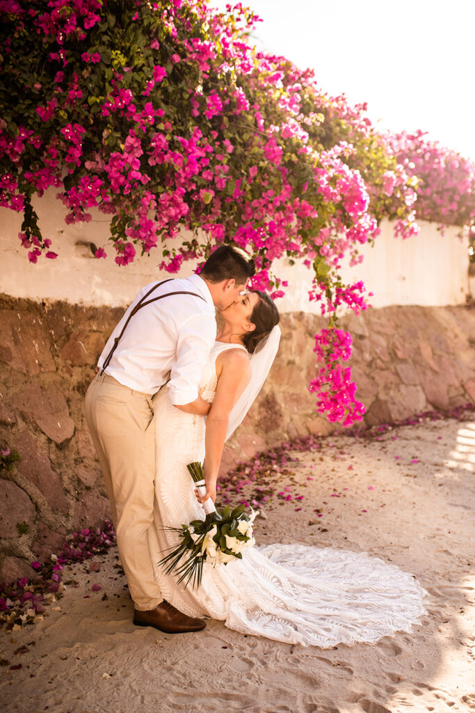 Newlyweds kissing surrounded by pink flowers in Cabo San Lucas